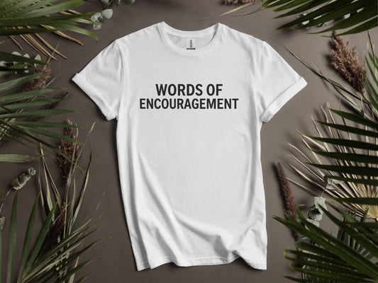 White t-shirt with "WORDS OF ENCOURAGEMENT" text, framed by dried plants.