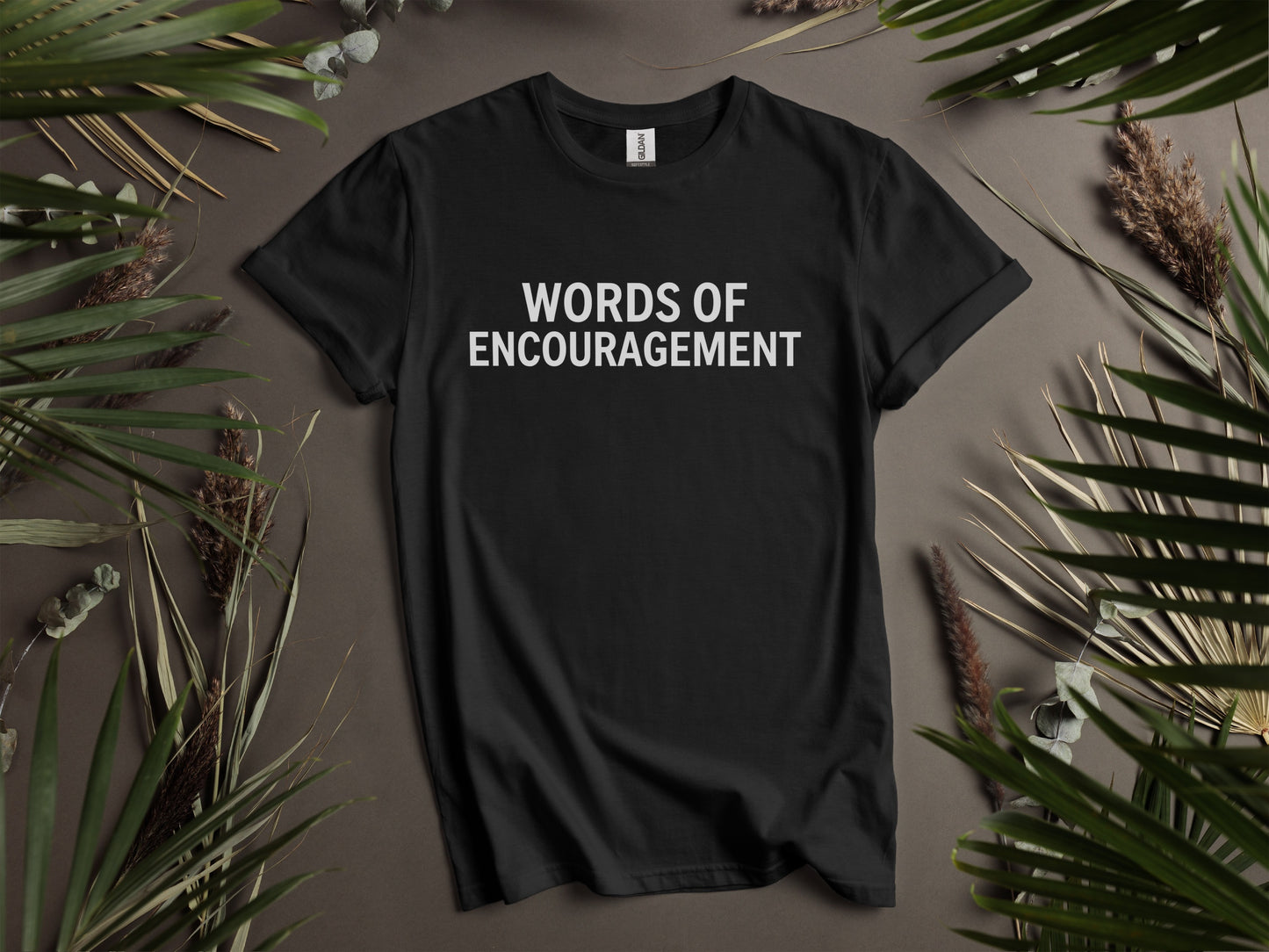 Black t-shirt with white text "WORDS OF ENCOURAGEMENT" and surrounding foliage.