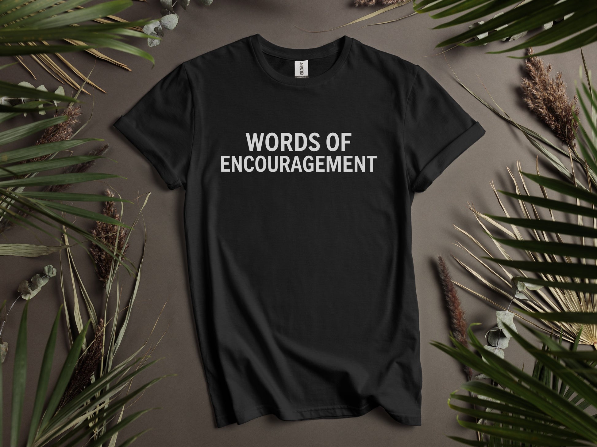 Black t-shirt with white text "WORDS OF ENCOURAGEMENT" and surrounding foliage.