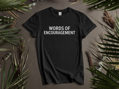Black t-shirt with white text "WORDS OF ENCOURAGEMENT" and surrounding foliage.